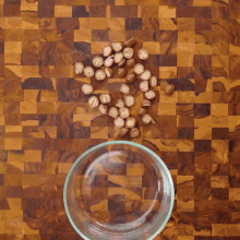 a person is holding a glass bowl filled with nuts on a wooden table .