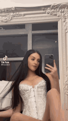 a woman in a white corset is taking a picture of herself in a mirror