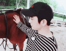 a man wearing a black hat and striped shirt petting a brown horse
