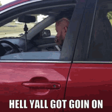 a man driving a red car with the words " hell yall got goin on " on the bottom