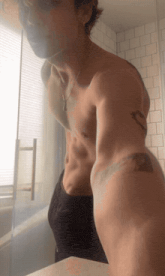 a shirtless man with a tattoo on his arm looks at himself in the mirror