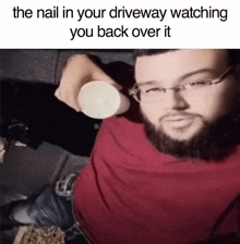 a man with glasses and a beard is holding a cup with the caption the nail in your driveway watching