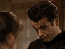 a man and a woman are looking at each other in a room and the man is smiling .