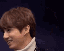 a close up of a young man wearing a turtleneck and earrings .