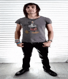 a young man wearing a mickey mouse t-shirt is standing with his hands in his pockets