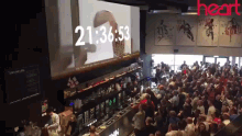 a crowd of people are gathered in front of a large screen that says 21 : 36 : 53 on it