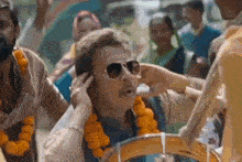 a man wearing sunglasses is covering his ears while playing a drum in a crowd .