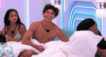 a group of people are laying on a bed including a shirtless man and two women