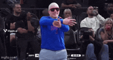 a man wearing sunglasses and a blue shirt is dancing in front of a crowd at a basketball game
