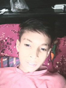 a young boy laying on a bed with a pink pillow