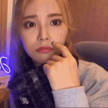 a woman with a scarf around her neck is making a funny face with her finger in her nose .