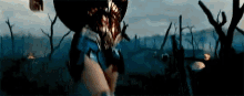 a woman in a superhero costume is standing in a field of dead trees