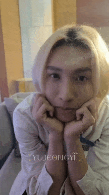a young man with blonde hair is making a funny face with his hands on his chin