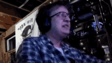 a man wearing a plaid shirt and glasses is sitting in front of a sign that says " ppa wit "
