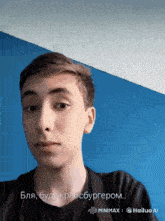 a young man in a black shirt is looking at the camera with a blue wall behind him