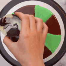 a person 's hand is holding a piece of cake with chocolate and green frosting on it