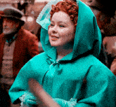 a woman with red hair is wearing a blue cape with a hood and smiling