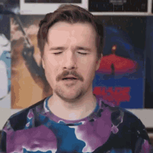 a man with a beard and mustache is wearing a tie dye shirt and making a funny face .