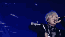 a man is singing into a microphone on a stage in front of a blue background .