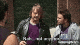 two men are standing next to each other on a sidewalk and one of them is talking to the other .