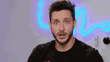 a man with a beard is making a funny face in front of a neon sign