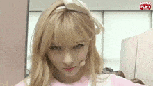 a girl with blonde hair is wearing a headband with a bow and a microphone in front of a minx play sign