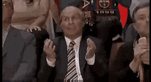 a man in a suit and tie is sitting in a stadium applauding .