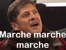 a man is making a funny face with his mouth open and the words marche marche marche on the screen behind him .