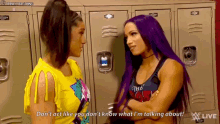 two women with purple hair are standing next to each other in front of lockers and talking to each other .