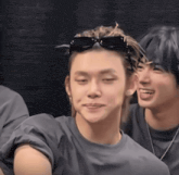 a man wearing sunglasses looks at the camera while another man smiles behind him