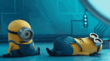 two minions are sitting on the floor and one is laying on the ground .