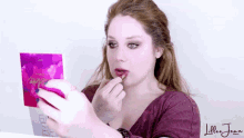 a woman is applying lipstick in front of a mirror with the name lillee joan on the bottom right