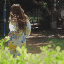 a woman in a floral robe is walking in a garden