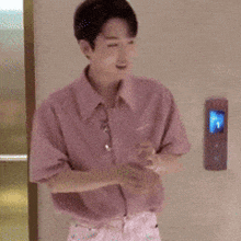 a man in a pink shirt is standing with his arms crossed in front of a door .