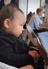 a baby wearing a black sweatshirt with the letter t on it sits in a chair