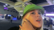 a woman wearing a green hat with a frog on it and the word al above her
