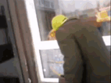 a man in a green coat and yellow hat is standing in front of a window .