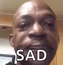 a bald man is crying and the word sad is on his face .