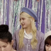 a blonde woman wearing a blue hat and a purple jacket