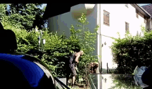 a man is standing in front of a house with a blue car in the foreground