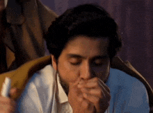 a man in a white shirt is coughing into his hand while another man holds a bottle of medicine .
