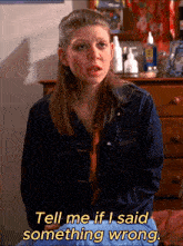a woman in a denim jacket is sitting on a bed and says tell me if i said something wrong