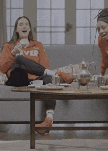 a woman in a fever sweatshirt sits on a couch next to a coffee table