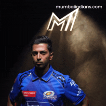 a man in a blue indians jersey stands in front of a sign that says mumbaiindians.com