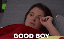 a woman is laying in bed with a red blanket and the words good boy above her