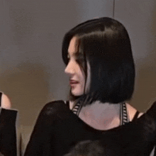 a woman with short black hair is wearing a black top and a bra .