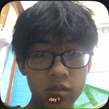 a young man wearing glasses has a day 1 button on his face