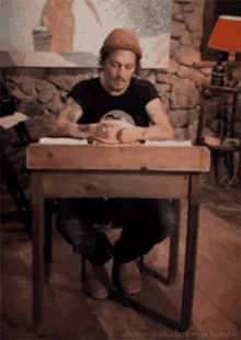 a man sits at a small wooden table with the words " theresinthedarkness.tumblr " on the bottom right
