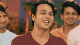 a man in a red shirt is smiling while standing in front of a group of men .