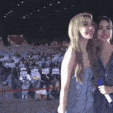 two women are standing next to each other in front of a crowd holding signs that say i love you .